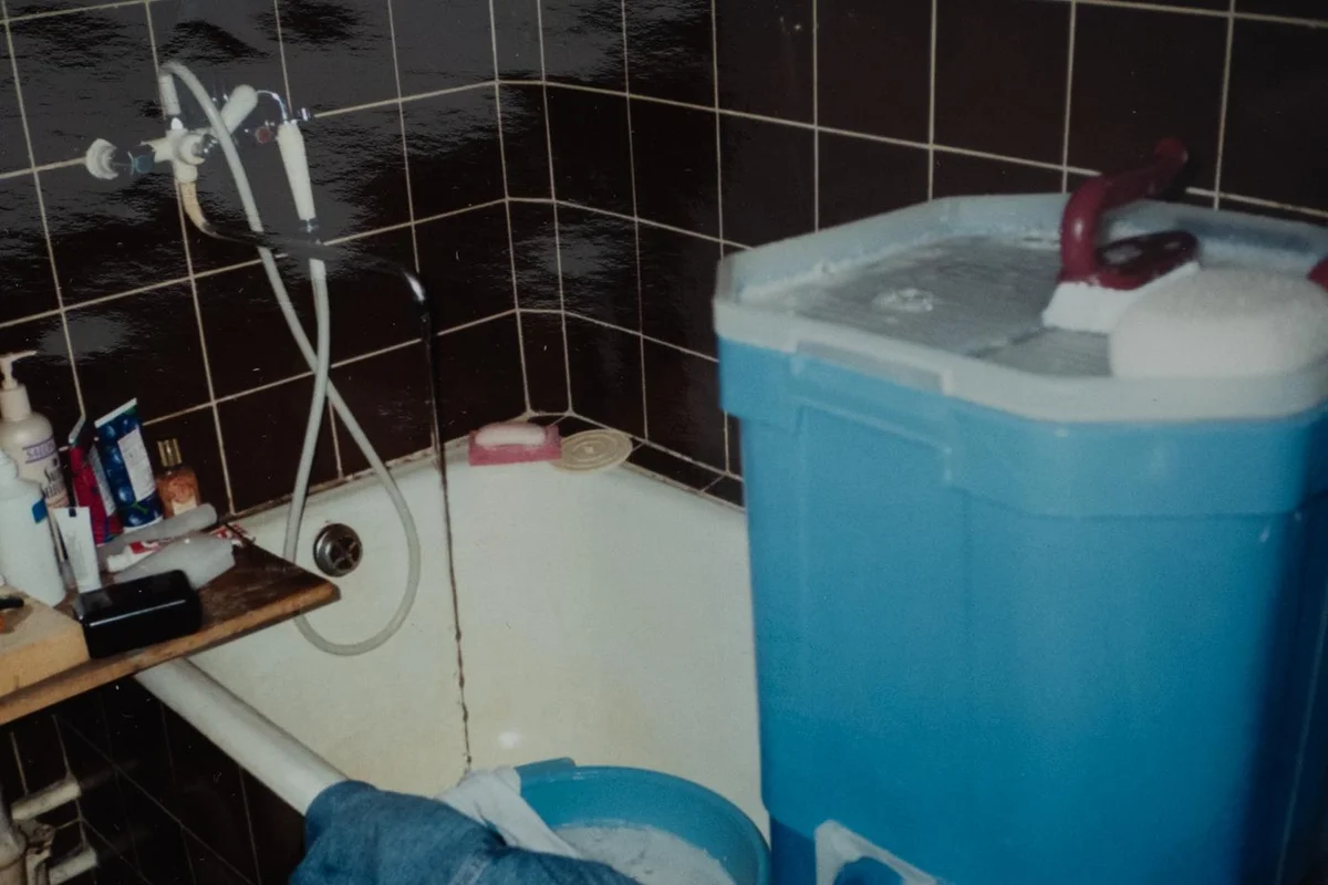 Narrow tiled bathroom with fixed faucet, tub, and small plastic storage bins