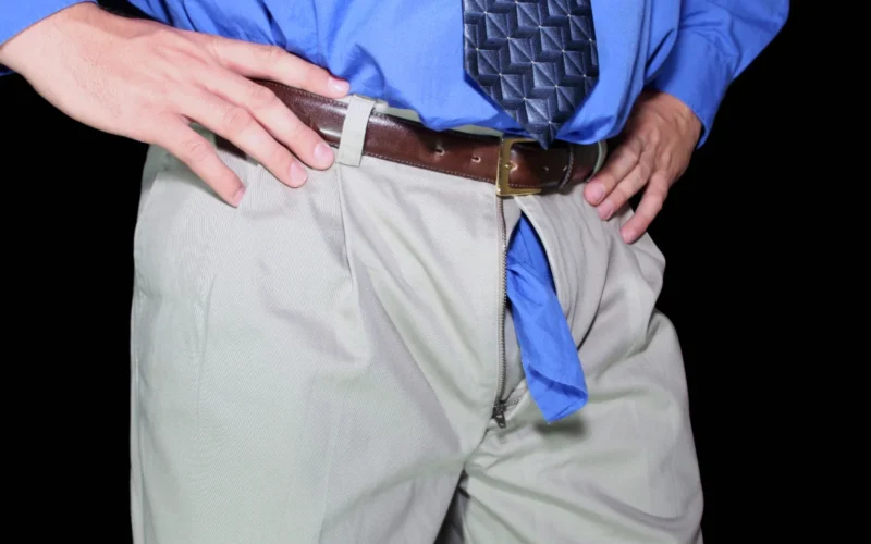 Man in blue shirt with open trouser zipper adjusting belt