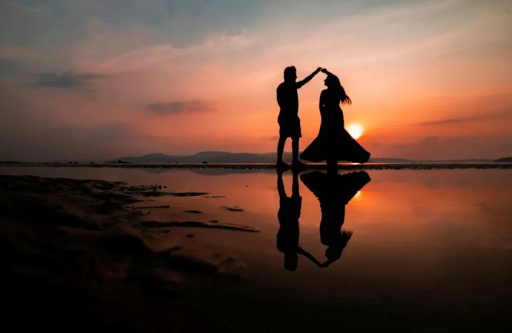 Silhouetted couple forming a heart shape with hands at sunset beach