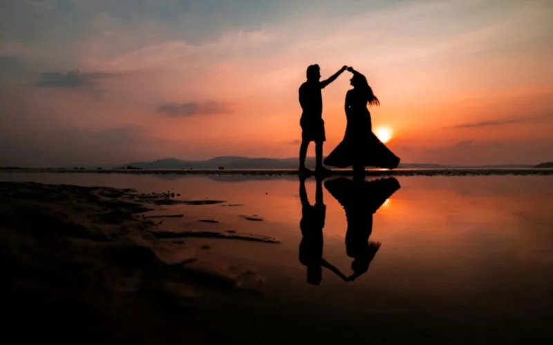 Silhouetted couple forming a heart shape with hands at sunset beach